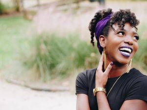Image of black woman laughing in front of plant.